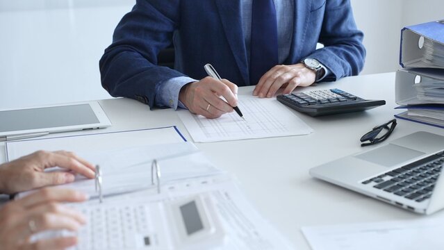Close up of female accountant hands using calculator while collaborating with male colleague in office, calculating taxes and analyzing financial data. Audit and taxes in business