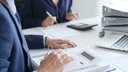 Close up of male accountant hands using calculator and collaborating with female colleague in a modern office, calculating taxes and analyzing financial data. Audit and taxes in business