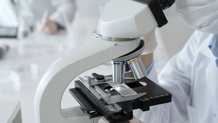 White gloved hands of scientist professional adjusting a microscope in a bright laboratory,...