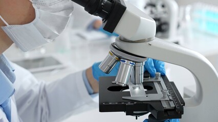Close up of scientific professional blue gloved hands examining microscope lens, performing...