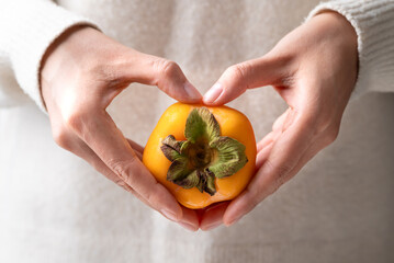 Fresh ripe persimmon holding by woman hand with heart shape, Autumn sweet fruit