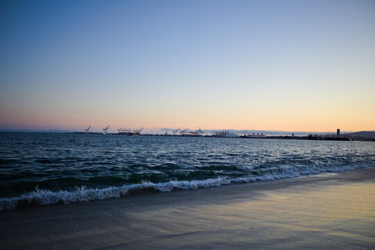 Tranquil sunset over Long Beach, California with soft waves, distant docks, and a glowing sky — capturing coastal serenity and the beauty of evening light.