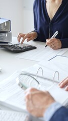 Business colleagues are reviewing financial reports and using a calculator during a productive...