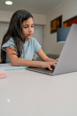 Young girl doing homework on laptop with mother's help at home
