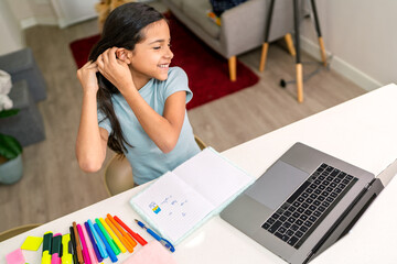 Latin girl doing homework and tying her hair at home