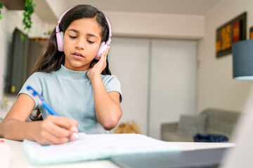 Young girl doing homework and listening music with headphones at home