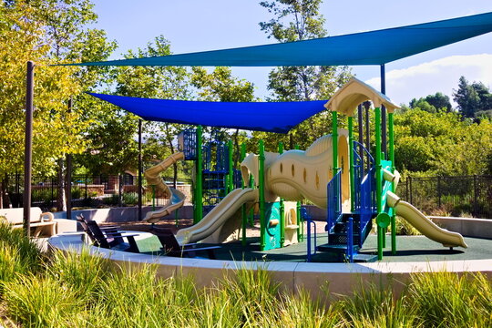 Colorful playground in Corona, California, featuring slides, shade covers, and play structures surrounded by trees in a sunny, family-friendly park setting.