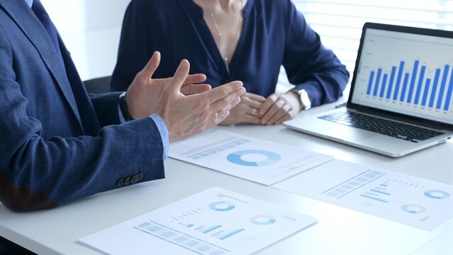 Businessman and business woman reviewing financial documents, collaborating over laptop screen, analyzing market charts for strategic corporate planning. Businesspeople and finance concept - Powered by Adobe