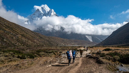 Porter carrying guest bags in Sagarmatha nationalpark in Nepal with beautiful view of Mt.Ama Dablam.