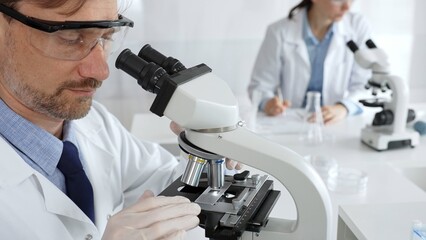 Researcher examining sample through microscope, wearing safety eyewear in sterile laboratory...