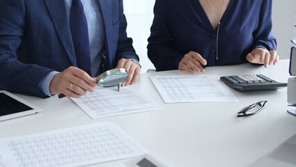 Professional accountants or auditors are analyzing financial reports with a magnifying glass and...