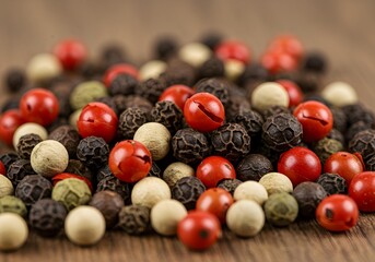 Vibrant assortment of whole black, white, green, and red peppercorns on a wooden background, a concept of spice variety