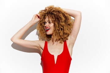Young woman with curly hair in a red swimsuit expressing joy against a white background, summer...