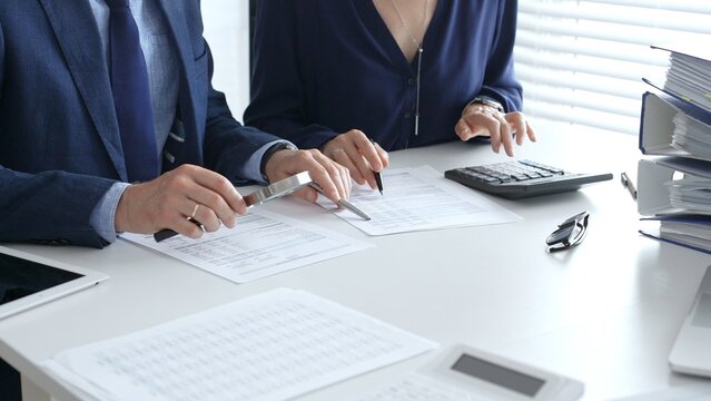 Chartered accountants analyzing financial reports with a magnifying glass and calculator for precise compliance verification. Audit and taxes in business - Powered by Adobe