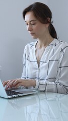 Professional businesswoman working intently on laptop, sitting at minimalist glass desk in bright...