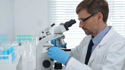 Medical scientist wearing gloves using microscope analyzing samples in modern laboratory doing scientific research. Medicine, healthcare and science concept