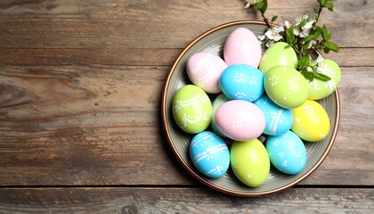 A decorative bowl brimming with colorful, patterned Easter eggs sits atop a weathered wooden surface, complemented by a delicate spring blossom branch.
