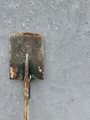 Vintage rusty shovel with wooden handle leaning on gray textured concrete wall background