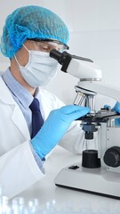Senior male scientist wearing a protective mask, cap, and gloves, examining samples under a microscope in a modern laboratory. Medicine, healthcare and science concept