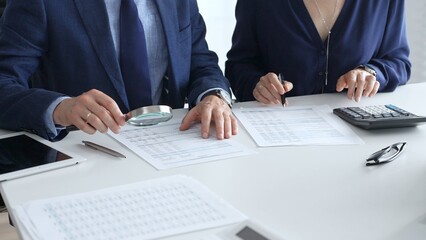 Chartered accountants analyzing financial reports with a magnifying glass and calculator for precise compliance verification. Audit and taxes in business