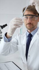 Scientist in lab coat and protective glasses analyzing green liquid in test tube with pipette in a professional laboratory. Medicine, health care and science concept