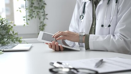 Female doctor in lab coat and stethoscope using digital tablet at desk in medical office, accessing online patient information. Medicine and health care concept - Powered by Adobe