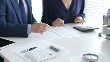 Close up of calculator and magnifying glass over financial documents opposite financial team analyzing data, reviewing reports, collaborating at modern office workspace. Audit and taxes in business - Powered by Adobe
