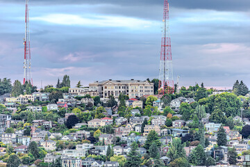 Fototapeta premium Colorful hillside neighborhood with dense houses, historic building, and tall red-white radio towers against a dramatic sky. Perfect stock image for urban landscapes, architecture, and city skylines.