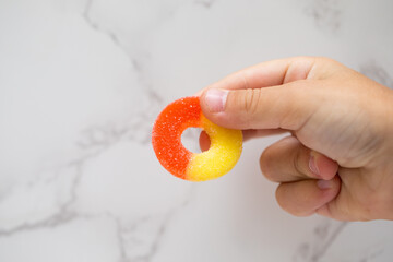 a young child hand's holding a sugar coated peach ring gummy candy on white background