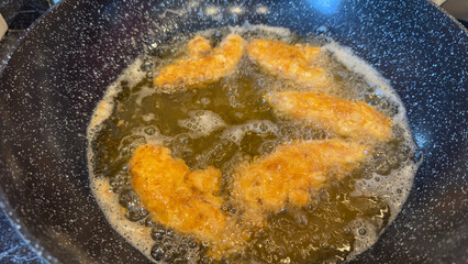 Breaded chicken strips deep frying in hot oil in a wok