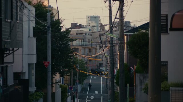 Tokyo Neighborhood Sunset with Power Lines Silhouetted Against Sky &ndash; Urban Tokyo street view with silhouetted power lines and glowing sky at sunset behind apartment buildings.