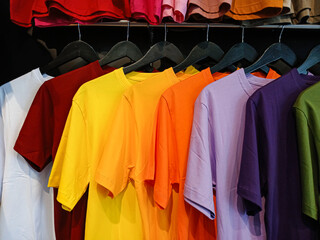 Obraz premium A variety of colorful plain t-shirts hanging on a rack. This vibrant rainbow of casual apparel is perfect for fashion, retail, and shopping concepts.