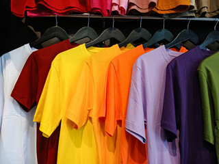 Obraz premium A variety of colorful plain t-shirts hanging on a rack. This vibrant rainbow of casual apparel is perfect for fashion, retail, and shopping concepts.