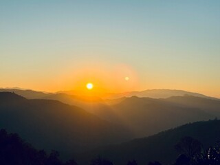 A breathtaking view of a vibrant golden sunset over rolling mountain ranges, with a beautiful lens flare effect.
