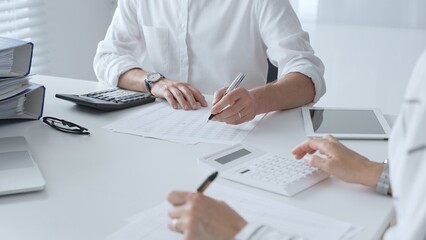Two unrecognizable accountants collaborating in a well lit office, analyzing financial data and...