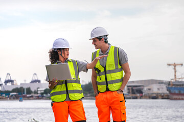 Diverse team of port engineers or logistics managers collaborating at a busy shipyard. They use a laptop and radio to coordinate cargo ship operations and manage the supply chain.