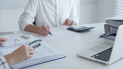 Team of accountants are working together, using a magnifying glass and a calculator, to audit...