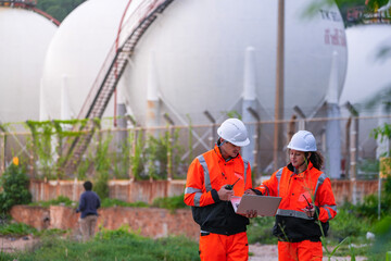 Two diverse engineers in safety gear collaborate with a laptop at a natural gas storage facility. A...