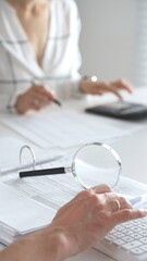 Two accountants are working together, using a magnifying glass and a calculator, to audit financial...