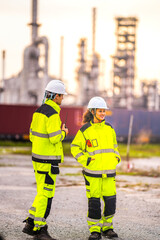 Two engineers in high-visibility safety gear and helmets conduct a field inspection at an industrial plant during sunrise, holding a tablet and measuring tools with soft pastel light background.
