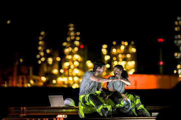 Two industrial workers take a break during the night shift at a construction site, sitting on steel...