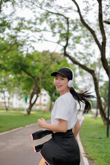Young Asian sportswoman running in the park listening to music with headphones