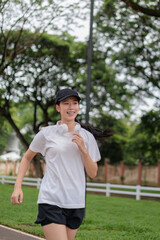 Young asian woman running in a park listening music with headphones