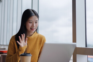 Young Asian Freelancer Woman Waving Hand During Video Call in Cafe