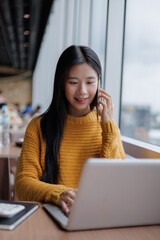 Young Asian Freelancer Working on Laptop and Talking on Phone in Cafe