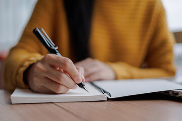 Woman writing notes on notebook with pen at wooden table