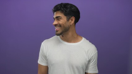 Young hispanic man wearing white tshirt turning head and smiling in purple studio with side profile view; confidence. - Powered by Adobe