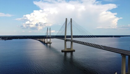 Wide shot of a cable-stayed bridge spanning a calm body of water under a partly cloudy sky