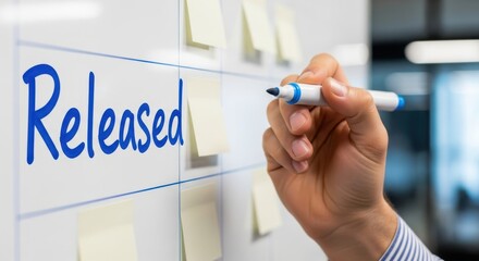 A hand writes the word released in blue marker on a whiteboard with sticky notes, signifying project completion and successful planning