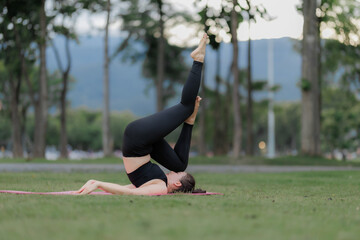 Fototapeta premium Asian woman practicing yoga peacefully in the park after work, finding relaxation and balance at sunset.